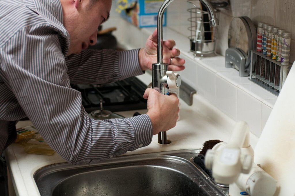 plumber's plunger and drain snake tool placed next to a kitchen sink