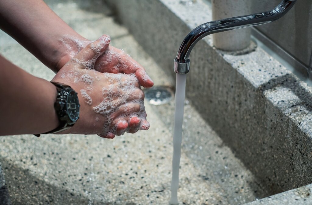 person gently rinsing air conditioner filter under lukewarm water